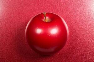 Vibrant red apple sits against matching glittery red background, The apple glossy surface reflects light, photo