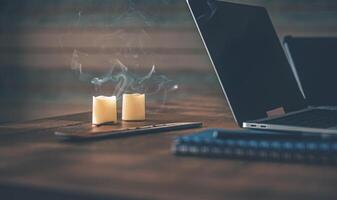 Home Office. On the table there is a laptop, a tablet, a blue notebook with a pen for notes, two candles and an incense stick photo