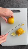 hands of woman cutting lemon into slices on white cutting board on grey concrete table, top view video