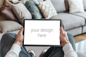 Tablet mockup. Person sits on sofa in room and holds tablet in front of him. psd