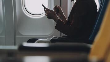 Woman hand using smart phone on airplane. Female traveler using smart phone in passenger cabin. Can be add your texts or others on screen. Sun shining trough airplane window. Technology concept. video