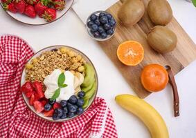 Granola with strawberries, kiwi, banana and blueberries in a round plate on a black table. Healthy and tasty food photo
