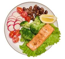 Healthy lunch with grilled trout on green lettuce, next to vegetables, tomatoes, radishes, broccoli and a portion of beans photo