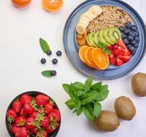 Granola with strawberries, kiwi, banana and blueberries in a round plate on a white table. Healthy and tasty food photo