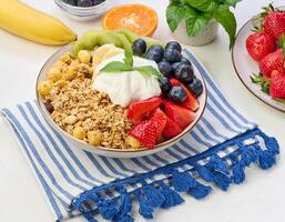 Granola with strawberries, kiwi, banana and blueberries in a round plate on a white table. photo