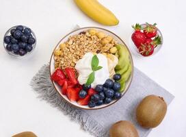 Granola with strawberries, kiwi, banana and blueberries in a round plate on a white table. photo