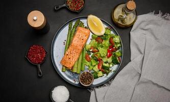 Healthy lunch with grilled trout with asparagus and fresh tomato and cucumber salad, a row of lemon slice. photo