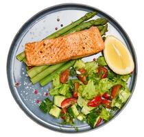 Healthy lunch with grilled trout with asparagus and fresh tomato and cucumber salad, a row of lemon slice. photo