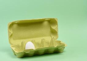 One white egg in a paper box on a green background photo