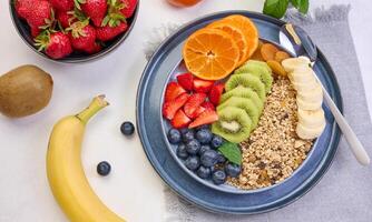 Granola with strawberries, kiwi, banana and blueberries in a round plate on a white table. photo