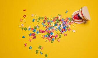 Artificial jaw with teeth, from which multi-colored letters of the alphabet spilled out on a yellow background photo