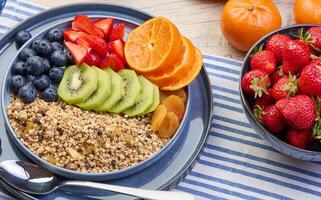 Granola with strawberries, kiwi, banana and blueberries in a round plate on a white table. photo