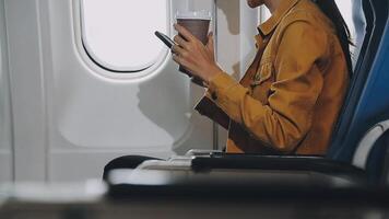 Woman hand using smart phone on airplane. Female traveler using smart phone in passenger cabin. Can be add your texts or others on screen. Sun shining trough airplane window. Technology concept. video