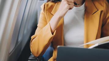Attractive asian female passenger of airplane sitting in comfortable seat listening music in earphones while working at modern laptop computer with mock up area using wireless connection on board. video