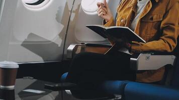 Attractive asian female passenger of airplane sitting in comfortable seat listening music in earphones while working at modern laptop computer with mock up area using wireless connection on board. video