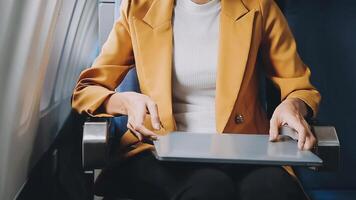 Attractive asian female passenger of airplane sitting in comfortable seat listening music in earphones while working at modern laptop computer with mock up area using wireless connection on board. video