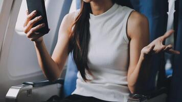Attractive asian female passenger of airplane sitting in comfortable seat listening music in earphones while working at modern laptop computer with mock up area using wireless connection on board. video