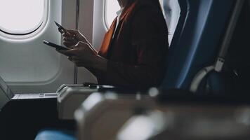 Attractive asian female passenger of airplane sitting in comfortable seat listening music in earphones while working at modern laptop computer with mock up area using wireless connection on board. video