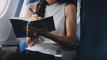 Attractive asian female passenger of airplane sitting in comfortable seat listening music in earphones while working at modern laptop computer with mock up area using wireless connection on board. video