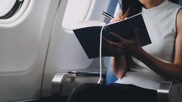 Attractive asian female passenger of airplane sitting in comfortable seat listening music in earphones while working at modern laptop computer with mock up area using wireless connection on board. video