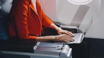 Attractive asian female passenger of airplane sitting in comfortable seat listening music in earphones while working at modern laptop computer with mock up area using wireless connection on board. video