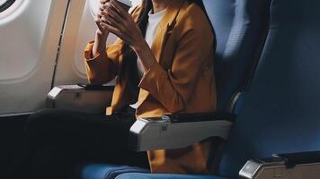 Attractive asian female passenger of airplane sitting in comfortable seat listening music in earphones while working at modern laptop computer with mock up area using wireless connection on board. video