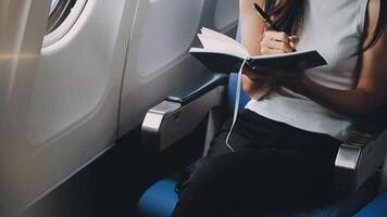 Attractive asian female passenger of airplane sitting in comfortable seat listening music in earphones while working at modern laptop computer with mock up area using wireless connection on board. video