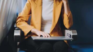 Attractive asian female passenger of airplane sitting in comfortable seat listening music in earphones while working at modern laptop computer with mock up area using wireless connection on board. video