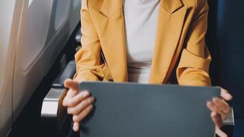 Attractive asian female passenger of airplane sitting in comfortable seat listening music in earphones while working at modern laptop computer with mock up area using wireless connection on board. video