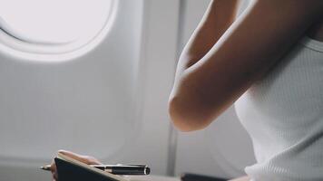 Attractive asian female passenger of airplane sitting in comfortable seat listening music in earphones while working at modern laptop computer with mock up area using wireless connection on board. video