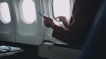 Woman hand using smart phone on airplane. Female traveler using smart phone in passenger cabin. Can be add your texts or others on screen. Sun shining trough airplane window. Technology concept. video