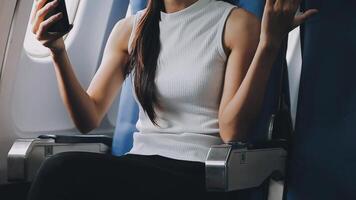 Attractive asian female passenger of airplane sitting in comfortable seat listening music in earphones while working at modern laptop computer with mock up area using wireless connection on board. video