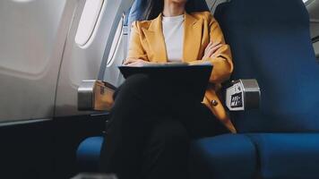 Attractive asian female passenger of airplane sitting in comfortable seat listening music in earphones while working at modern laptop computer with mock up area using wireless connection on board. video