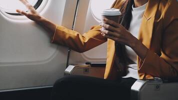 Attractive asian female passenger of airplane sitting in comfortable seat listening music in earphones while working at modern laptop computer with mock up area using wireless connection on board. video