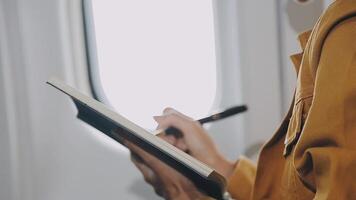 Attractive asian female passenger of airplane sitting in comfortable seat listening music in earphones while working at modern laptop computer with mock up area using wireless connection on board. video