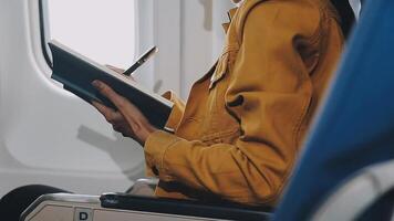 Attractive asian female passenger of airplane sitting in comfortable seat listening music in earphones while working at modern laptop computer with mock up area using wireless connection on board. video