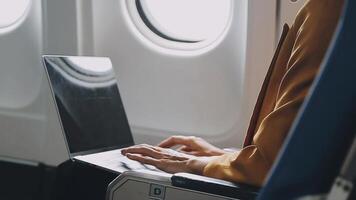 Attractive asian female passenger of airplane sitting in comfortable seat listening music in earphones while working at modern laptop computer with mock up area using wireless connection on board. video