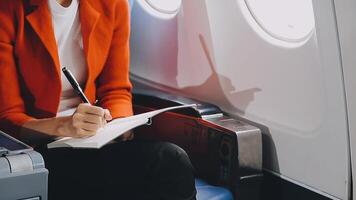 Attractive asian female passenger of airplane sitting in comfortable seat listening music in earphones while working at modern laptop computer with mock up area using wireless connection on board. video