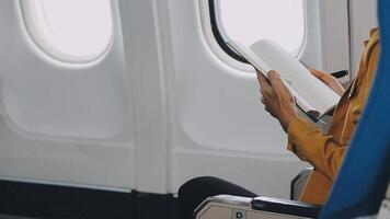 Attractive asian female passenger of airplane sitting in comfortable seat listening music in earphones while working at modern laptop computer with mock up area using wireless connection on board. video