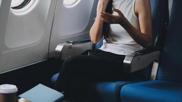 Attractive asian female passenger of airplane sitting in comfortable seat listening music in earphones while working at modern laptop computer with mock up area using wireless connection on board. video