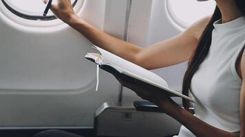 Attractive asian female passenger of airplane sitting in comfortable seat listening music in earphones while working at modern laptop computer with mock up area using wireless connection on board. video