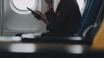 Woman hand using smart phone on airplane. Female traveler using smart phone in passenger cabin. Can be add your texts or others on screen. Sun shining trough airplane window. Technology concept. video
