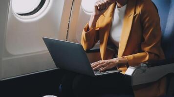 Attractive asian female passenger of airplane sitting in comfortable seat listening music in earphones while working at modern laptop computer with mock up area using wireless connection on board. video