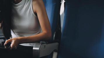 Attractive asian female passenger of airplane sitting in comfortable seat listening music in earphones while working at modern laptop computer with mock up area using wireless connection on board. video