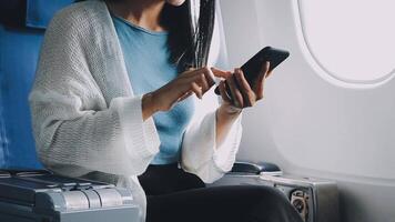Woman hand using smart phone on airplane. Female traveler using smart phone in passenger cabin. Can be add your texts or others on screen. Sun shining trough airplane window. Technology concept. video