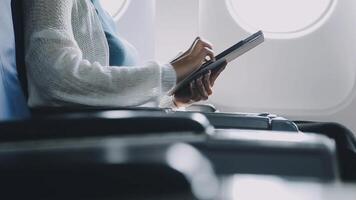 Attractive asian female passenger of airplane sitting in comfortable seat listening music in earphones while working at modern laptop computer with mock up area using wireless connection on board. video