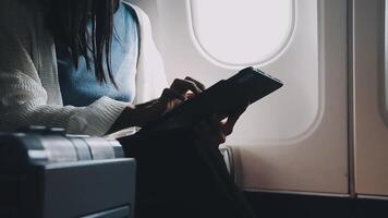 Attractive asian female passenger of airplane sitting in comfortable seat listening music in earphones while working at modern laptop computer with mock up area using wireless connection on board. video