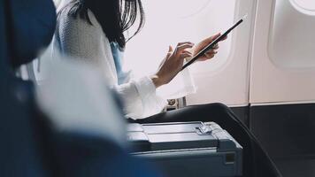 Attractive asian female passenger of airplane sitting in comfortable seat listening music in earphones while working at modern laptop computer with mock up area using wireless connection on board. video