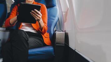 Attractive asian female passenger of airplane sitting in comfortable seat listening music in earphones while working at modern laptop computer with mock up area using wireless connection on board. video