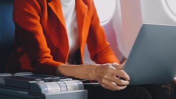 Attractive asian female passenger of airplane sitting in comfortable seat listening music in earphones while working at modern laptop computer with mock up area using wireless connection on board. video